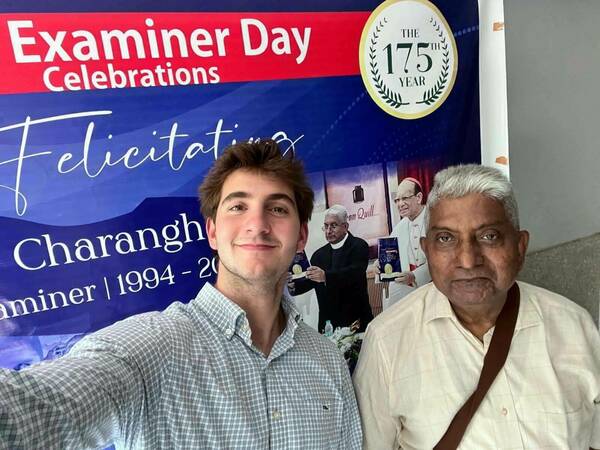 Fr. Tony and Andrew pose in front of a poster commemorating the 175th anniversary of the Examiner.