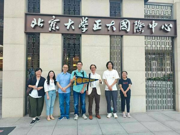 Seven people stand smiling before the Peking University Notre Dame International Center in China. One person holds a small University of Notre Dame pennant.