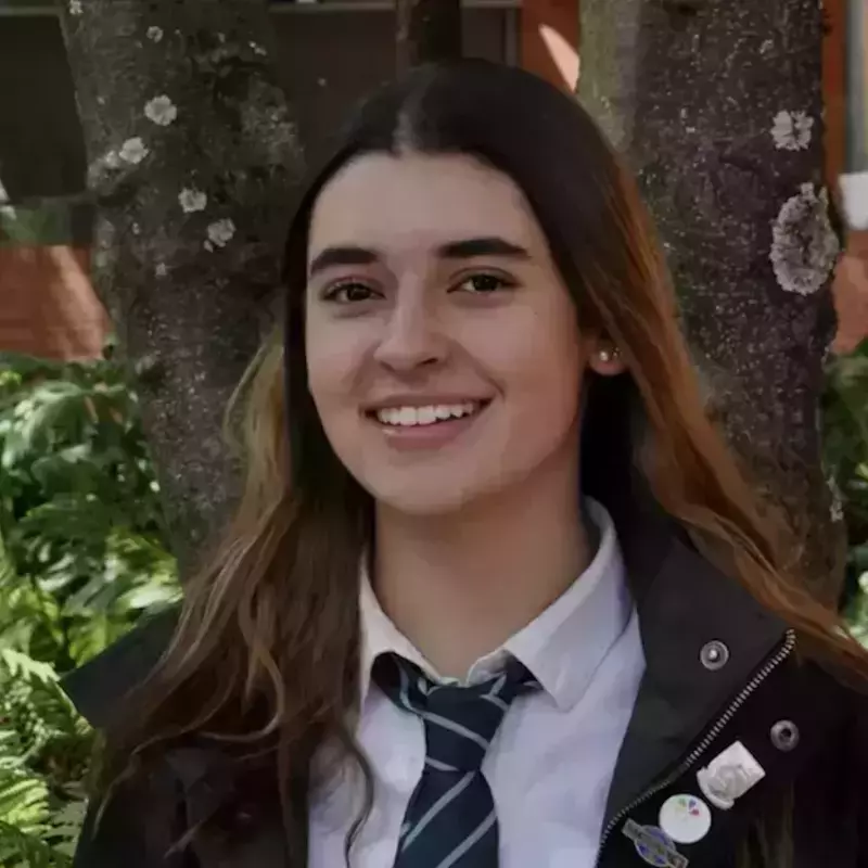 Maria Antonia Gaviria Caicedo. A young woman with long dark hair smiles broadly, wearing a white shirt, a green and white striped tie, and a dark jacket, with trees in the background.