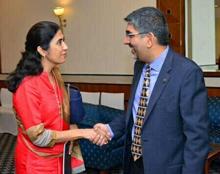 Woman in red tunic shakes hands with broadly smiling man in blue suit and patterned tie.