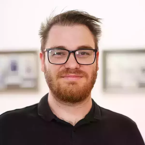 Dr. Nathan Steinmeyer. Man with reddish-brown beard, black-framed glasses, and a black polo shirt smiles faintly.