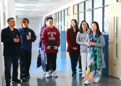 A group of eight students and adults walk and smile brightly in a sunlit hallway. One wears a Notre Dame jacket.