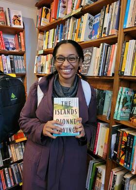 Dionne Irving holds her book, "The Islands," surrounded by bookshelves.