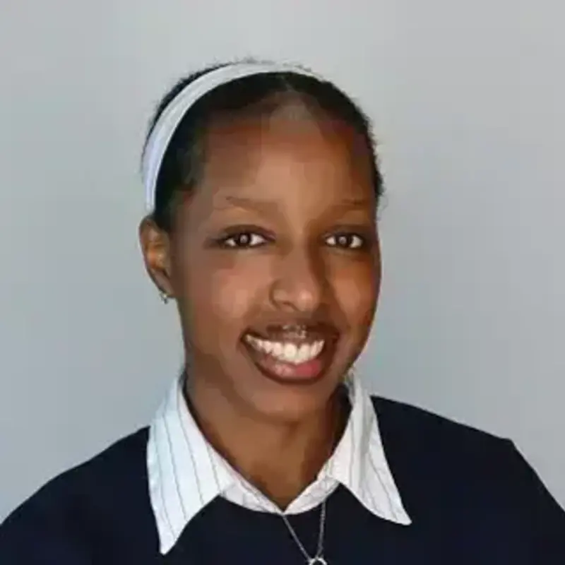 Karen Keza. Young Black woman smiling, wearing a white headband and a blue sweater over a striped shirt.