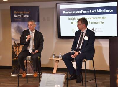 Two men in suits sit at a Notre Dame "Ukraine Impact Forum: Faith & Resilience" panel. One speaks into a mic.