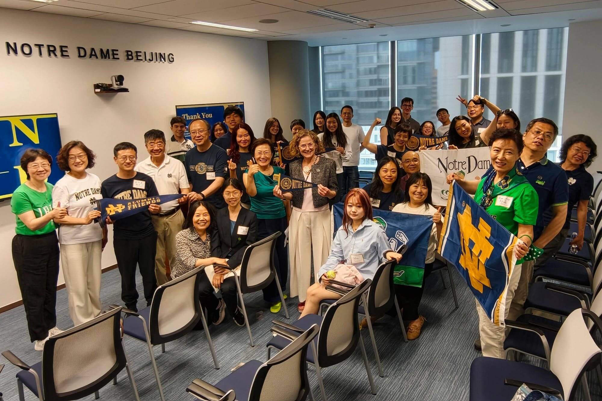 Smiling Notre Dame alumni and friends pose at Notre Dame Beijing, holding blue & gold flags and pennants.