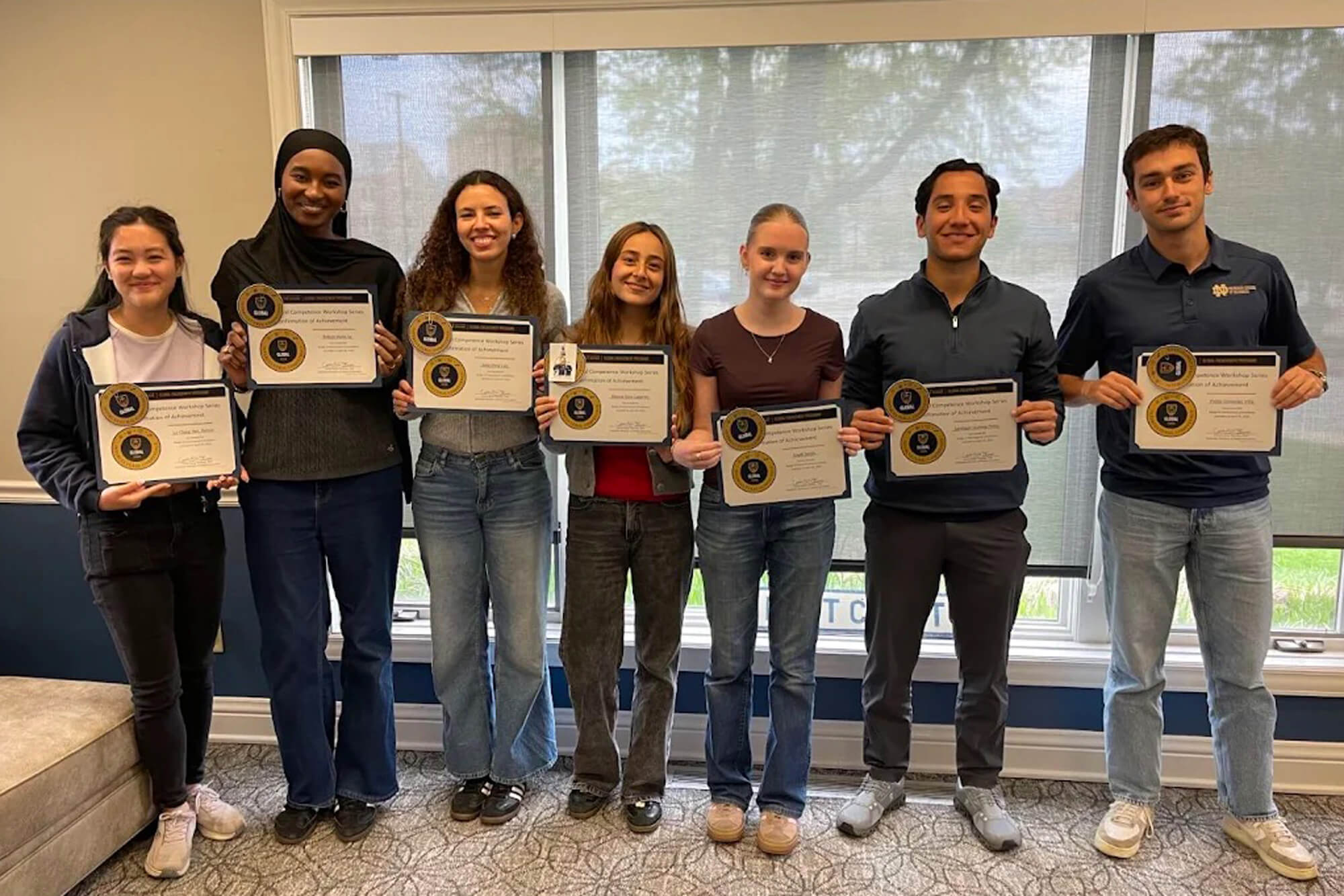 Seven smiling students, 4 women and 3 men, proudly hold GLOBAL Competency Workshop Series certificates of achievement.