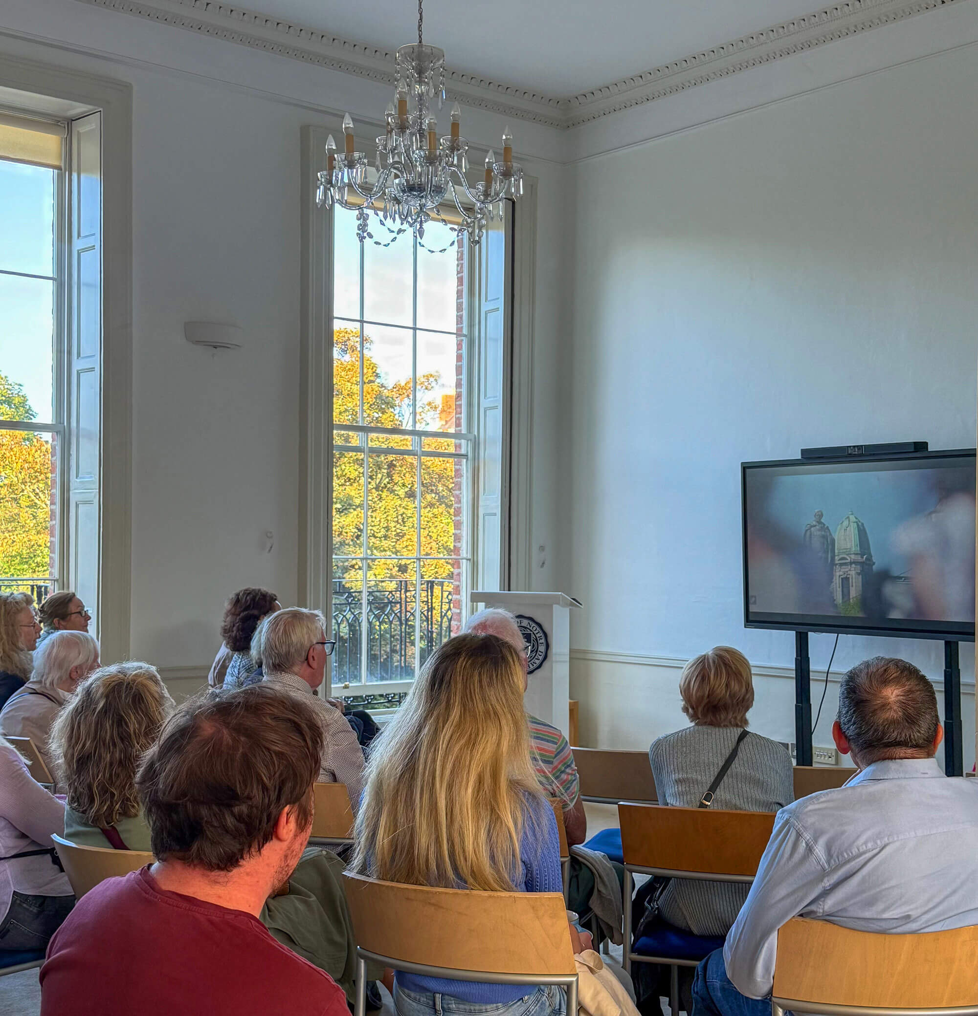 Audience watches a presentation with an image of a dome and statue on a large screen.