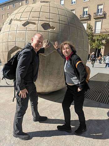 Man in black and woman in black with striped shirt lean on globe sculpture.