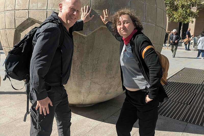 Man in black and woman in black with striped shirt lean on globe sculpture.