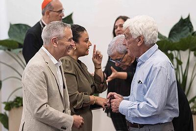 Two men and two women converse in a room with green plants.